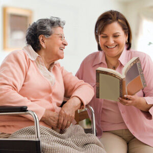 A woman and an older person are smiling while reading.